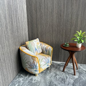May include: Miniature living room set with a patterned armchair, matching pillow, and a small round table. The armchair has a yellow trim and the table is dark brown. A small plant and a cup and saucer are on the table.