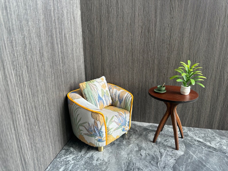 May include: Miniature living room set with a patterned armchair, matching pillow, and a small round table. The armchair has a yellow trim and the table is dark brown. A small plant and a cup and saucer are on the table.