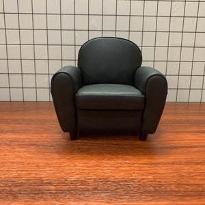 May include: A black leather armchair with a rounded back and rolled arms. The chair is sitting on a wooden floor.