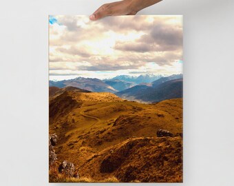 Könnte beinhalten: Ein rechteckiger Leinwanddruck mit einer Landschaftsaufnahme von goldbraunen Hügeln und einem gewundenen Feldweg, der zu fernen, schneebedeckten Berggipfeln unter einem mit weißen und grauen Wolken bedeckten Himmel bei Tageslicht führt.