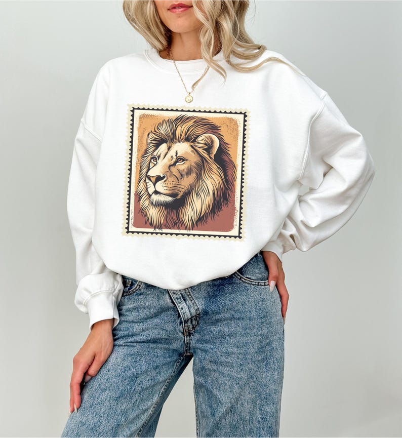 K&ouml;nnte beinhalten: Wei&szlig;er Pullover mit einem Aufdruck eines L&ouml;wenkopfes in einem Vintage-Briefmarken-Design. Der L&ouml;we ist braun und hat eine wei&szlig;e M&auml;hne.