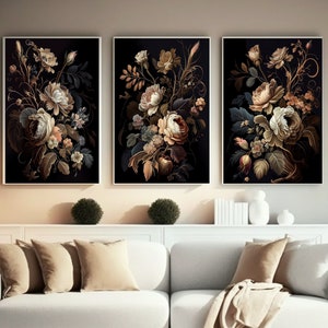 May include: Three framed floral art prints. Each features a dark background with a detailed arrangement of cream, peach, and gold flowers. The artwork is displayed above a white sofa with beige pillows and a throw blanket.