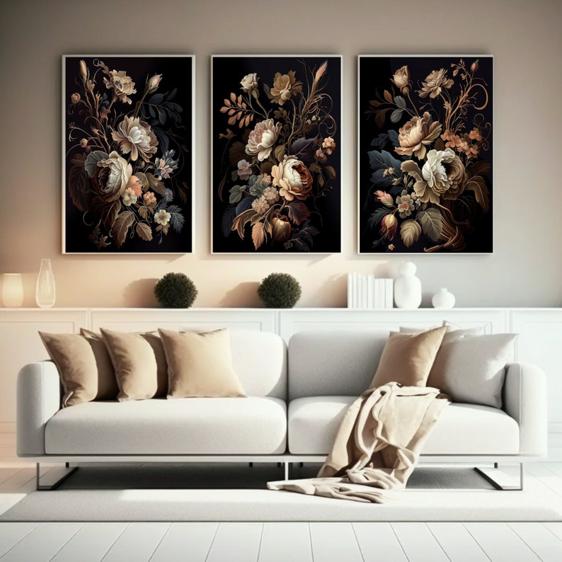 May include: Three framed floral art prints. Each features a dark background with a detailed arrangement of cream, peach, and gold flowers. The artwork is displayed above a white sofa with beige pillows and a throw blanket.