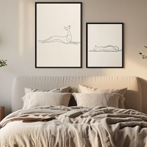 Peut inclure: Deux impressions d'art encadrées avec des dessins au trait minimalistes de chats. Le dessin au trait noir est posé sur un fond crème, avec un cadre noir. La plus grande impression montre un chat en position assise, tandis que la plus petite représente un chat couché.