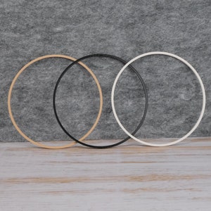 Op de afbeelding: Drie hoepels, een beige, een zwart en een wit, zijn op elkaar gestapeld. De hoepels zijn gemaakt van een dun, flexibel materiaal.