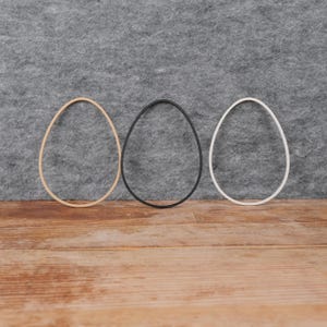 Op de afbeelding: Drie houten eivormige hoepels in beige, zwart en wit, gerangschikt in een rij op een houten oppervlak.