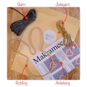 Op de afbeelding: Een macramé knutselset met grijs garen, jute touw, houten hartvormen en instructies. De set bevat een papieren zak en een gids met het woord "Makramee".