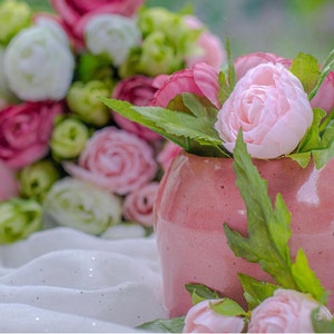 Puede incluir: Un jarrón de cerámica rosa con una superficie texturizada, lleno de flores artificiales rosas y blancas y hojas verdes.
