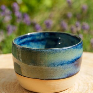 Peut inclure: Un petit bol en céramique avec une base beige lisse non émaillée et une finition en émail réactif brillant sur la partie supérieure. L'émail présente un dégradé de bleu marine profond au bord passant à un vert sauge clair et moucheté.