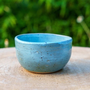 Peut inclure: Un petit bol en céramique bleu clair avec un glaçage moucheté. Le bol est posé sur une surface en bois.