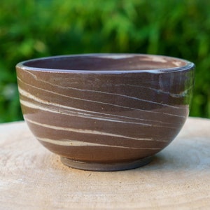 Peut inclure: Un bol en céramique brun avec des lignes blanches tourbillonnantes. Le bol est posé sur une surface en bois.