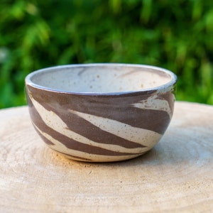 May include: A white ceramic bowl with brown stripes and speckles. The bowl is sitting on a wooden surface.