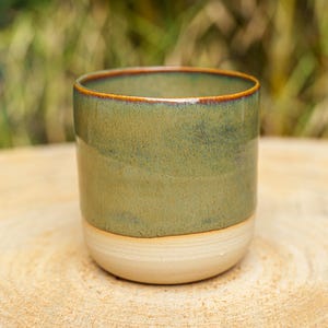 Groene keramische pot. Groen-bruine aardewerken pot. Houder voor een handgegoten kaars, eveneens van aardewerk.