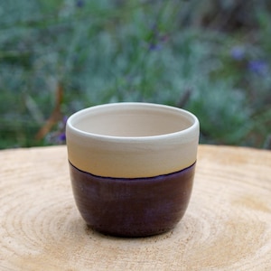 May include: A ceramic mug with a white top, a light yellow band, and a dark purple bottom.
