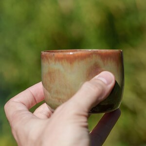 Könnte beinhalten: Eine kleine, handgefertigte Keramikschale mit einer grün-braunen Glasur. Die Schale wird in einer Hand gehalten.