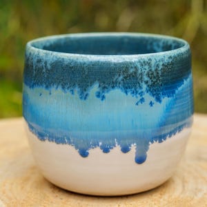 Peut inclure: Un mug en céramique présentant une silhouette arrondie et lisse avec une finition brillante. La partie supérieure affiche un vernis bleu marine profond qui se transforme en turquoise vif, créant un effet de coulure sur la base blanche.