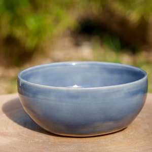 Peut inclure: Un bol en céramique bleu avec une finition lisse et brillante. Le bol est rond et a une légère lèvre autour du bord.