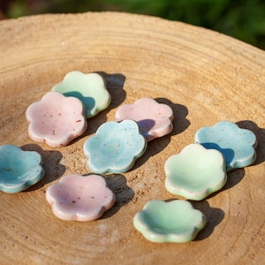 Peut inclure: Une collection de petits plats en céramique en forme de fleur dans des tons de rose, bleu et vert. Les plats sont disposés sur une surface en bois.