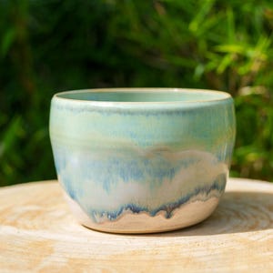 Può includere: Una piccola ciotola in ceramica rotonda con uno smalto liscio e lucido che sfuma da un delicato verde menta sul bordo a una miscela di azzurro, bianco e blu marino scuro verso la base, caratterizzata da un motivo fluido a goccia.