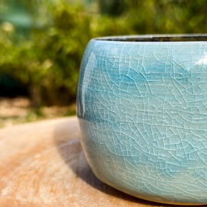 Könnte beinhalten: Eine hellblaue Keramikschale mit einer craquelé-Glasur. Die Schale hat eine runde Form und eine glatte, leicht strukturierte Oberfläche.