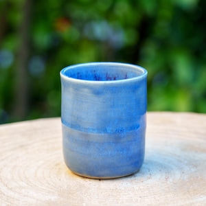 Puede incluir: Una taza de cerámica azul con un esmalte azul claro. La taza está sobre una superficie de madera.
