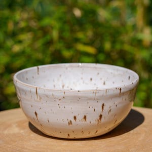Peut inclure: Un bol en céramique blanche avec des taches brunes. Le bol est posé sur une surface en bois.