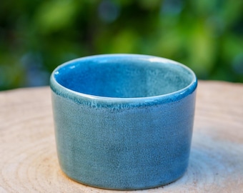 May include: A small, light blue ceramic bowl with a textured glaze. The bowl is sitting on a wooden surface.