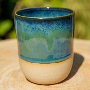 Peut inclure: Un gobelet en céramique cylindrique doté d'une base beige lisse non émaillée qui se transforme en un vernis goutte à goutte bleu profond et vert forêt brillant sur le dessus. Le bord est sombre et le vernis présente des variations de couleur.