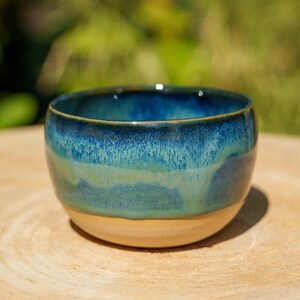 Könnte beinhalten: Eine kleine Keramikschale mit abgerundeter Form und einer glänzenden Glasur, die von einem tiefen Marineblau am Rand zu einem helleren Türkis und Blaugrün in der Mitte übergeht und in einem glatten, unglasierten beigen Boden endet.