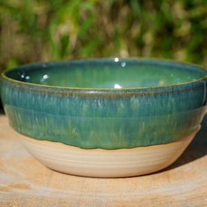 Peut inclure: Un bol en céramique fait à la main avec un glaçage bicolore. La partie supérieure est d'un vert-bleu vibrant, passant à un beige plus clair à la base. Le bord du bol a un bord plus foncé et contrasté. Idéal pour servir des aliments.
