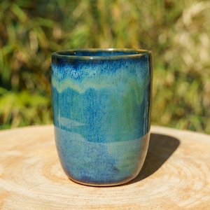 Peut inclure: Un gobelet cylindrique en céramique doté d'un vernis brillant aux nuances mélangées de bleu marine profond, de turquoise vibrant et de vert sauge doux. La surface présente une finition lisse et réfléchissante avec des dégradés subtils.