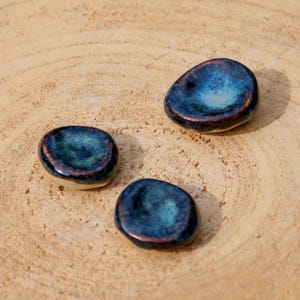 Peut inclure: Trois petits plats ronds en céramique avec un glaçage bleu foncé et un léger reflet métallique. Les plats sont disposés sur une surface en bois brun clair.