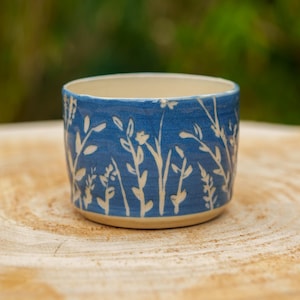 May include: A white ceramic mug with a black handle and the text "But First, Coffee" in a bold, black font. The mug is set against a blurred background, highlighting its clean design.