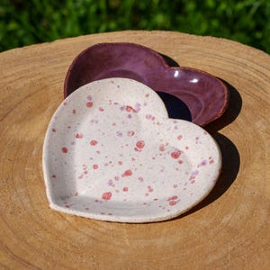 Op de afbeelding: Twee hartvormige keramische schalen. De bovenste schaal is diep paars. De onderste schaal is wit met roze stippen.