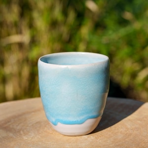 May include: A light blue ceramic cup with a white rim. The cup is sitting on a wooden surface.