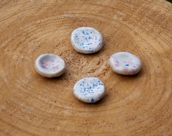 May include: Four small white ceramic dishes with blue and pink speckles. The dishes are arranged in a square pattern on a wooden surface.