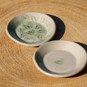 May include: Two ceramic dishes, one with a green leaf pattern and the other plain white, both with a subtle glaze.