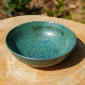 Könnte beinhalten: Handgefertigte Keramikschale mit türkisfarbener und blauer Glasur. Die Schale hat eine runde Form und steht auf einer Holzoberfläche. Das Innere weist ein Spiralmuster auf. Diese dekorative Schale eignet sich zum Servieren von Speisen oder als Dekoration.