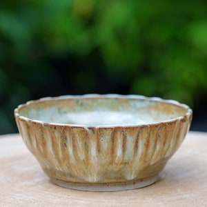 Peut inclure: Un bol en céramique avec un glaçage brun clair et un bord texturé et ondulé. Le bol est posé sur une surface en bois.