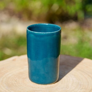 Peut inclure: Une tasse en céramique bleu sarcelle avec une finition lisse et brillante. La tasse est posée sur une surface en bois.