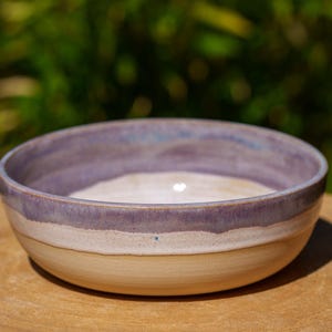 Peut inclure: Un petit bol en céramique blanche avec un glaçage violet et blanc. Le bol est posé sur une surface en bois.