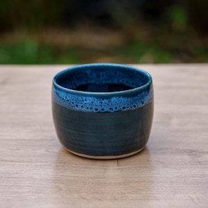 Könnte beinhalten: Eine kleine, dunkelblaue Keramikschüssel mit einem hellblauen Rand. Die Schüssel hat eine gesprenkelte Glasur und eine abgerundete Form.