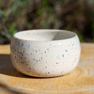 Kleiner weißer Keramikkugeltopf mit blauem Steingutkonfetti. Kleiner Steingutkeramiktopf mit weißem Konfetti. Topf in Form eines Baumwollschwanzes. Handgefertigte Keramik.