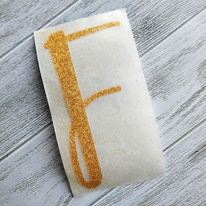 May include: Gold glitter letter F decal. The letter is on a white background.
