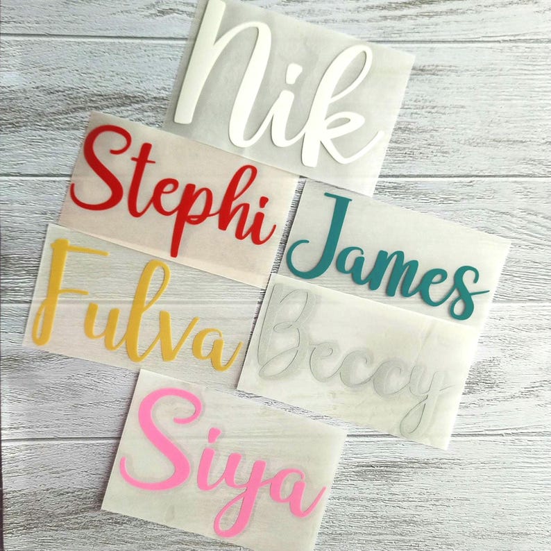 May include: A collection of vinyl name decals in various colors, including white, red, yellow, teal, pink, and gray. Each name is displayed in a cursive font on a transparent backing. The names include "Nik", "Stephi", "Fulva", "James", "Beccy", and "Siya".