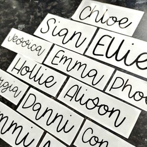 May include: White labels with black cursive writing, spelling out the names: Jessica, Hollie, Danni,  Sian, Ellie, Chloe, Emma, Alison,  Pho,  Gigi,  Con,  and  Ami.