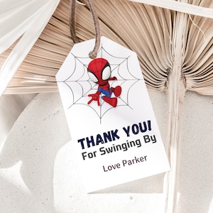 May include: A white thank you tag with a red and blue cartoon Spiderman character hanging from a web. The tag says "Thank You! For Swinging By Love Parker".