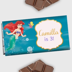 May include: A chocolate bar wrapper featuring Ariel, the Little Mermaid, with a gold frame and the text "Camilla is 3!"