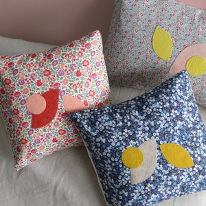 Könnte beinhalten: Drei dekorative Kissen mit Blumenmustern und Stoffapplikationen. Die Kissen haben verschiedene Farben und Muster, darunter Rot, Rosa, Gelb, Blau und Weiß.