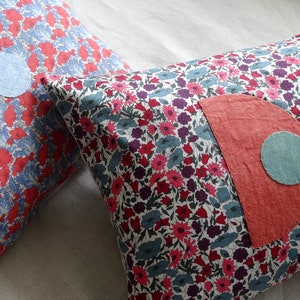 Peut inclure: Deux coussins décoratifs avec des motifs floraux. Un coussin a un motif floral bleu et rouge avec des cercles en tissu bleu. L'autre coussin a un fond blanc avec des fleurs rouges, roses et bleues et un demi-cercle en tissu rouge avec un cercle en tissu bleu.